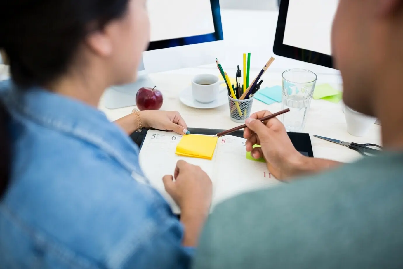 Ein männlicher Grafikdesigner und eine Grafikdesignerin schreiben in ein Tagebuch.