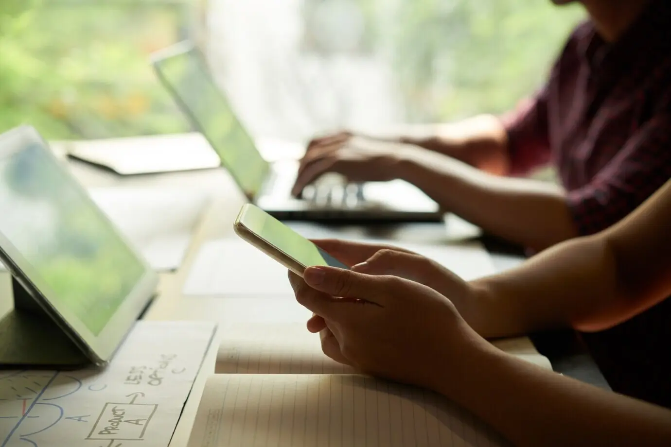 Hände einer Geschäftsperson beim gemeinsamen Prüfen von Nachrichten auf dem Smartphone mit einem Kollegen.